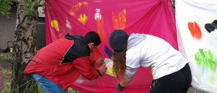 Two people photographed from behind spray painting a bike onto a pink sheet using a stencil