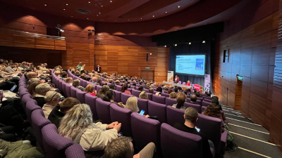 A photo from the back of a busy lecture room with Nicola and Kez presenting at the front