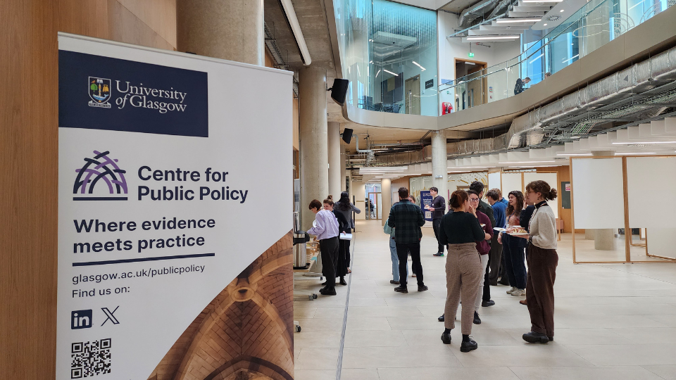 A photo of a crowd of people in conversation next to a Centre for Public Policy banner