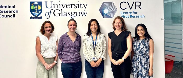 A group of five people standing in front of a wall with logos and text. The logos include the University of Glasgow, CVR Centre for Virus Research, and Medical Research Council.