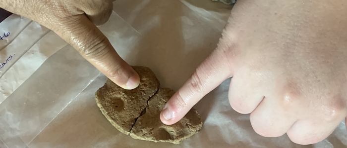 Two people touching indentations on a small piece of pottery with their little fingers