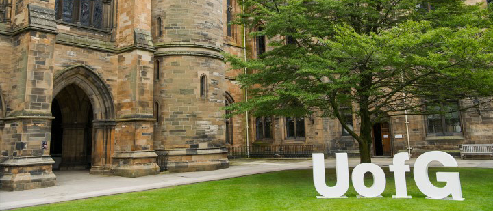 A large courtyard enclosed by stone walls with letters spelling UofG in the foreground